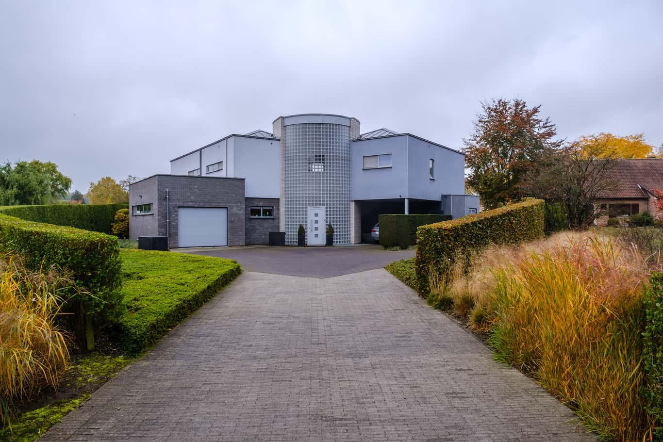 het huis van Roeland een speels huis is, dat aan een stapel blokken laat denken.nIn de voortuin hebben we vierkante blokken als dobbelstenen uitgerold. Aan de laatste dobbelsteen stroomt er water aan de voordeur. De woning is een speelse opstelling van blokken. Er wordt spanning opgebouwd in de voortuin. De hagen zijn eerst laag maar worden groter en groter.